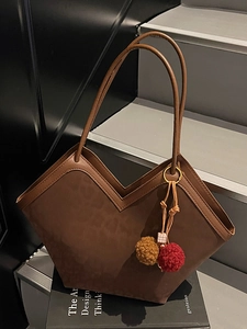 Brown leopard-style tote bag with V-shaped opening and pompom charm on black book prop