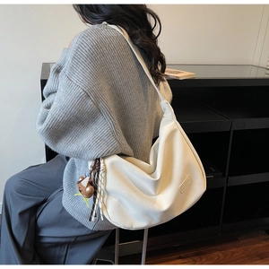 Détail du sac hobo beige souple avec bandoulière large, nœud tressé et charm ours