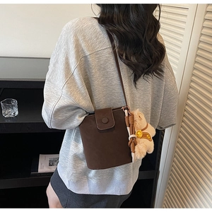 Détail du sac seau marron foncé avec texture mate et charmant pendentif d'ours en peluche
