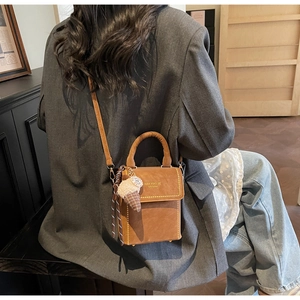 Detail of dark brown leather handbag featuring top handle and cute ice cream charm