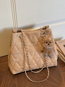 Chic beige quilted tote bag with gold chain strap and plush puppy charm on wood floor