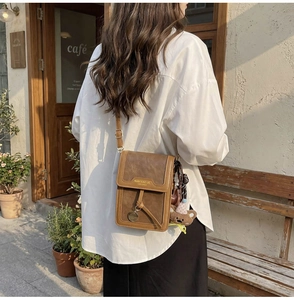 Close-up of brown leather crossbody phone bag with cute bear charm in street style