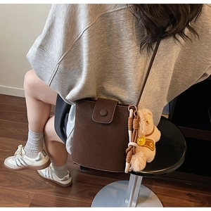 Détail du sac seau en cuir mat marron foncé avec un petit pendentif de poupée en peluche