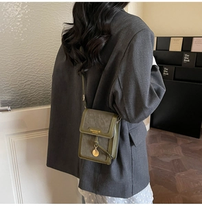 Close-up of small dark green leather crossbody bag with gold lettering and charm