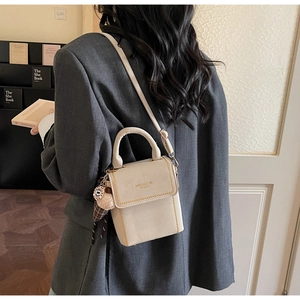 Detail of beige suede crossbody bag with gold stitching and decorative plush ball charm