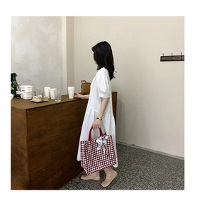 Detail of red houndstooth tote bag with decorative floral scarf handle and white dress