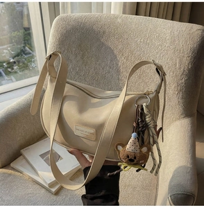 Detail of beige half-moon bag on sofa with cute bear pendant and leather brand tag
