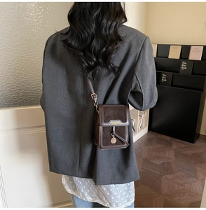 Close-up of a brown small crossbody bag with metal pendant shown on a model