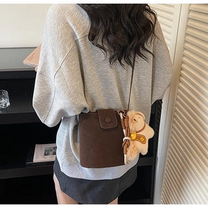Détail d'un sac seau en daim marron foncé avec fermeture à pression et breloque en peluche