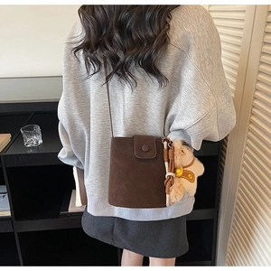 Vue détaillée du sac seau marron foncé mat avec un joli pendentif ours en peluche