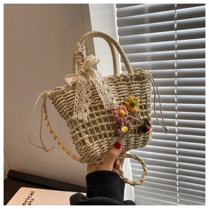 Detail of straw woven bucket bag with floral decorations and a delicate white lace bow