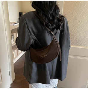 Detail of dark brown suede crescent bag with gold logo on adjustable shoulder strap