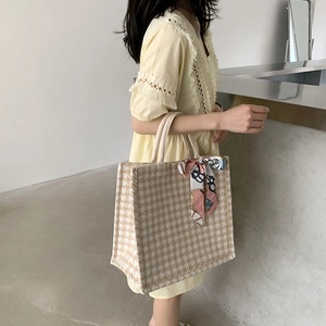 Detail of large houndstooth tote bag with pink silk scarf on handle worn by model