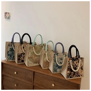Close-up of linen tote bags with vintage floral prints and pearl chain handles on a cabinet
