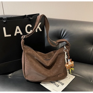 Vue détaillée du grand sac hobo marron rétro avec breloque ours sur fond en cuir noir