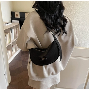 Detail of black matte croissant shoulder bag with gold metal logo and zipper on model