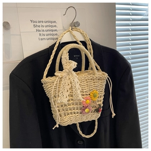 Detail of straw woven bucket bag featuring floral embroidery, ladybug charm, and lace tie