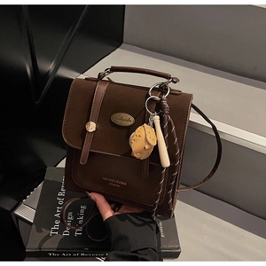 Detail van donkerbruine retro leren crossbodytas met een beerbedeltje en metalen plaatje