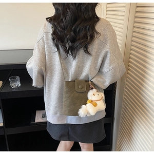 Détail du sac seau vert foncé avec breloque ours, porté par un mannequin en mode décontracté