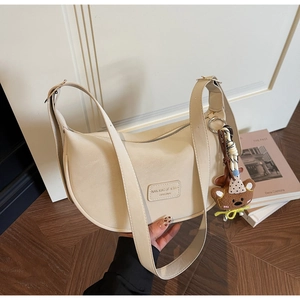 Detail of cream dumpling bag showing pebble leather texture and a cute plush bear charm