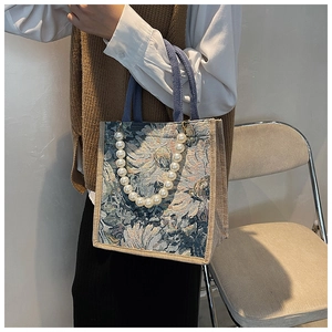 Detail of floral tapestry tote bag featuring large pearl strap and blue fabric handles