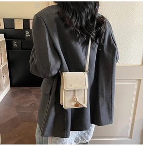 Vertical beige crossbody phone bag with tassel and logo shown on model in casual setting
