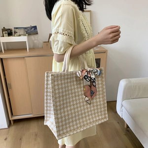 Detail of checkered canvas tote bag featuring decorative silk scarf and woven handles