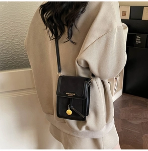 Detail of a black matte crossbody phone bag featuring a gold pendant and branding
