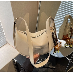 Detail view of beige crescent bag with adjustable strap and cute plush charms