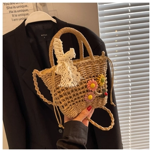 Detail of woven straw bucket bag featuring pink floral accents and lace bow detail
