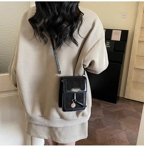 Close-up of black crossbody bag featuring gold logo and circular pendant in use