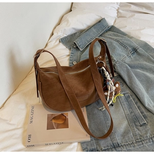 Detail of brown hobo bag with adjustable strap and decorative bear charm on white bedding
