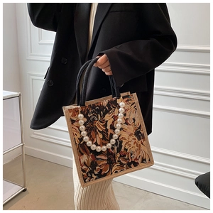 Chic tote bag with floral patterns and pearl embellishments carried by a model