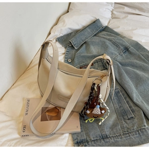 Detailed view of off-white dumpling bag with teddy bear charm and woven rope on soft bedding