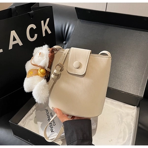 Détail du sac seau beige avec breloque ours en peluche et sangle dans une boîte cadeau
