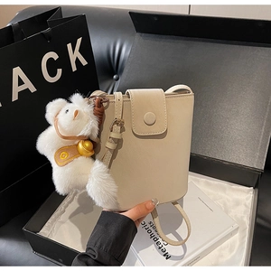 Détail du sac seau beige avec charme d'ours en peluche dans une boîte cadeau noire