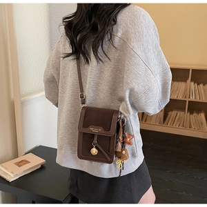 Detail of a brown small crossbody bag with gold charms and branded flap closure