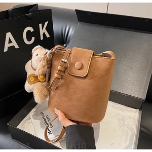 Détail du sac seau marron avec charm de chien en peluche et ferrures dorées en boîte cadeau