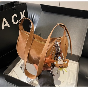 Close-up of brown leather dumpling hobo bag with teddy bear and starfish charms in a gift box