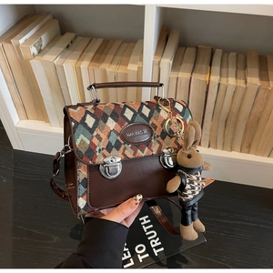 Détail du rabat en tissu à losanges sur un sac en cuir marron avec breloque lapin