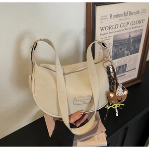 Detail of beige hobo bag with wide strap, leather logo tag and cute brown bear charm