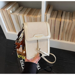 Close-up of minimalist cream leather phone bag with metal branding and cute charms