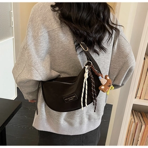 Detail of dark brown crescent bag with brand label and plush bear keychain accessory
