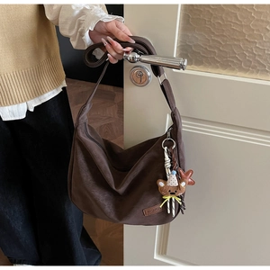 Détail du sac bandoulière marron en daim avec étiquette de mode et petit ours