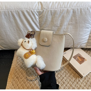 Détail d'un sac seau blanc crème avec un charme de cheval en peluche et rabat