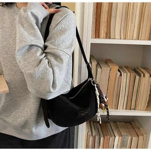 Detail of black moon-shaped hobo bag with woven charm on a model in a library