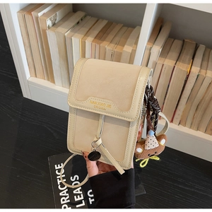 Close-up of cream crossbody phone bag with brown bear keychain and brand text details