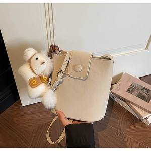 Détail d'un sac seau en cuir beige avec un charm en peluche doux et une fine bandoulière