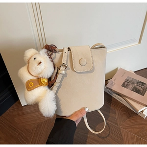 Détail d'un sac seau crème avec un pendentif ours en peluche et une finition mate lisse