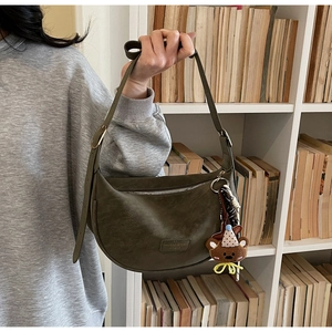 Close-up of a dark green dumpling shoulder bag with a bear charm and silver zipper